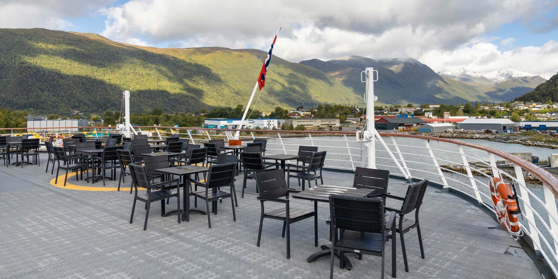 Black chairs and tables on outside deck onboard MS Fram, sea and mountains in the background.